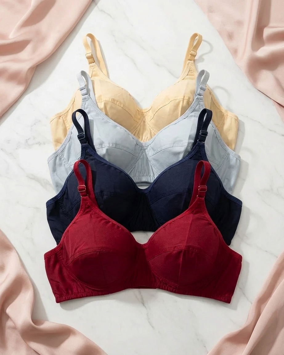 Three wireless underwire bras in navy blue, light gray, and deep red, arranged in a vertical stack on a white marble surface with draped pink satin fabric in the corners.