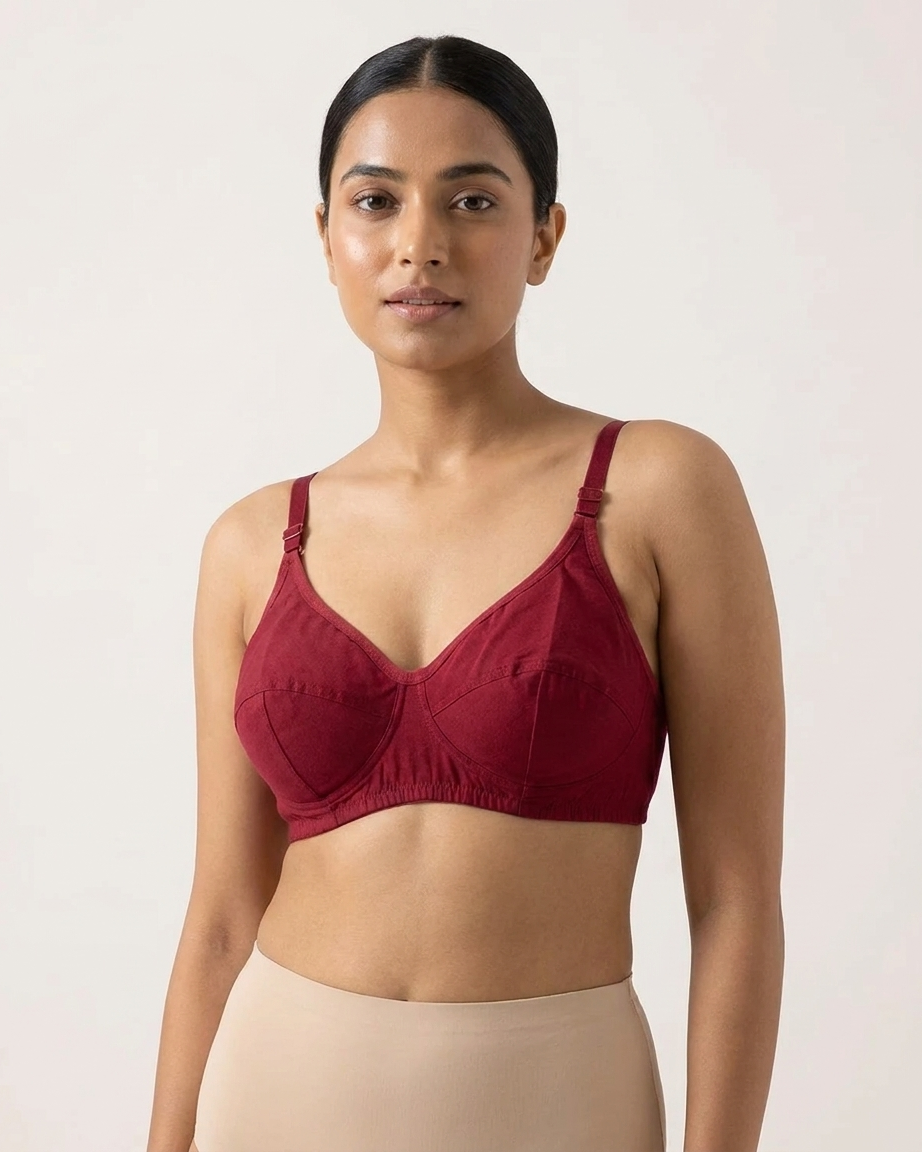 A woman modeling a deep burgundy underwire bra with structured cups and thin adjustable shoulder straps, paired with beige high-waisted shapewear bottoms, against a plain off-white studio background.